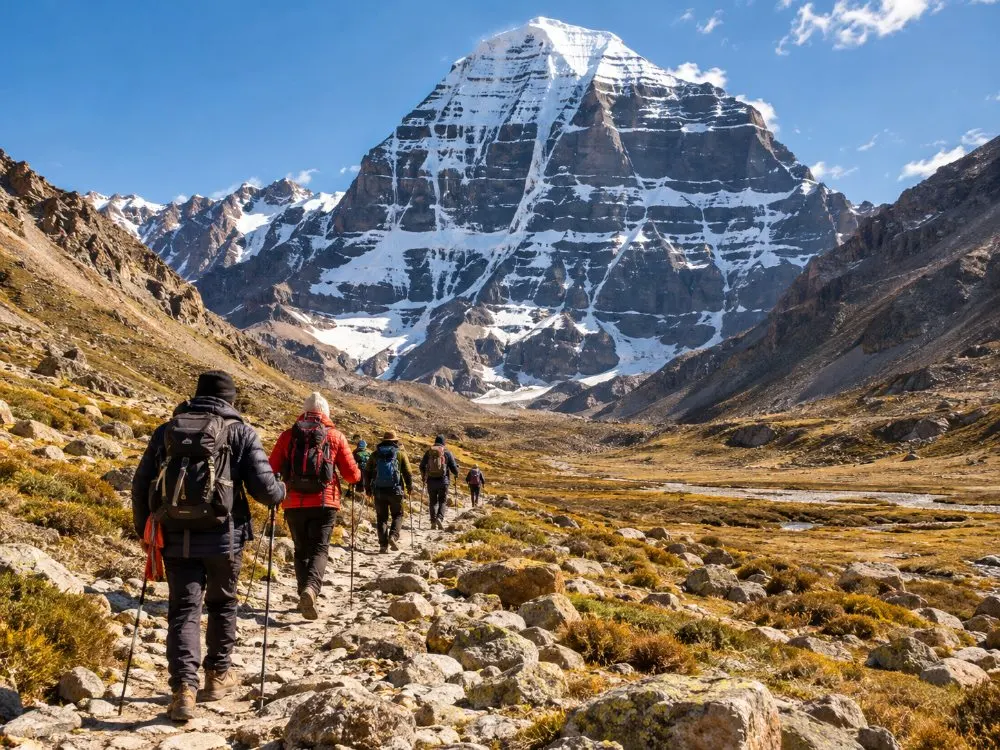 Des pèlerins en vestes chaudes marchant sur le sentier pierreux du kora sous la face nord sombre du Kailash